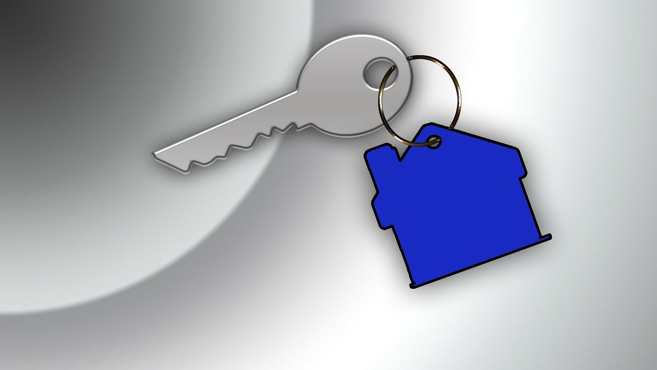 Image of metal key with a blue house keychain. This is on a grey background.